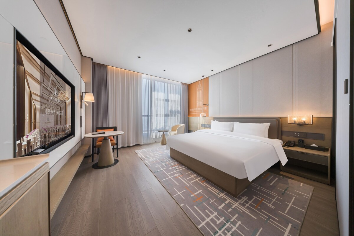 Una habitación de hotel moderna con una cama grande, un escritorio, una silla y una mesita.