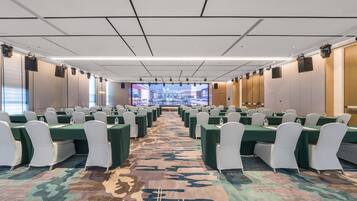 Une salle de conférence avec des rangées de tables et de chaises, un grand écran à l’avant et une moquette à motifs.