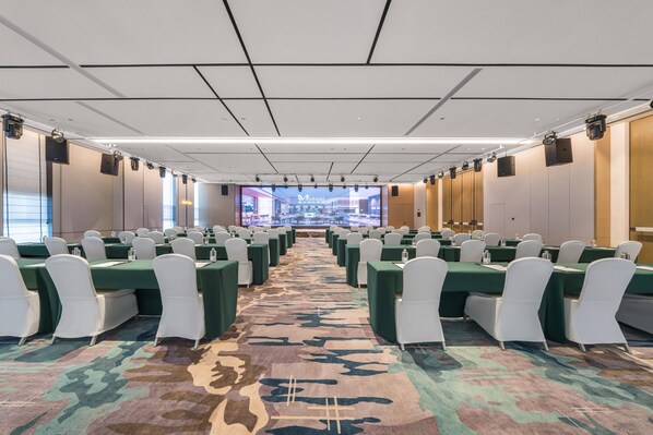 A conference room with rows of tables and chairs, a large screen at the front, and a patterned carpet. - Grand Madison Hotel Xiangyang Hexin Outlets (Xiangyang)