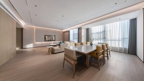 Uma sala de conferência moderna com uma mesa grande, várias cadeiras, um sofá e um amplo janelão com cortinas.
