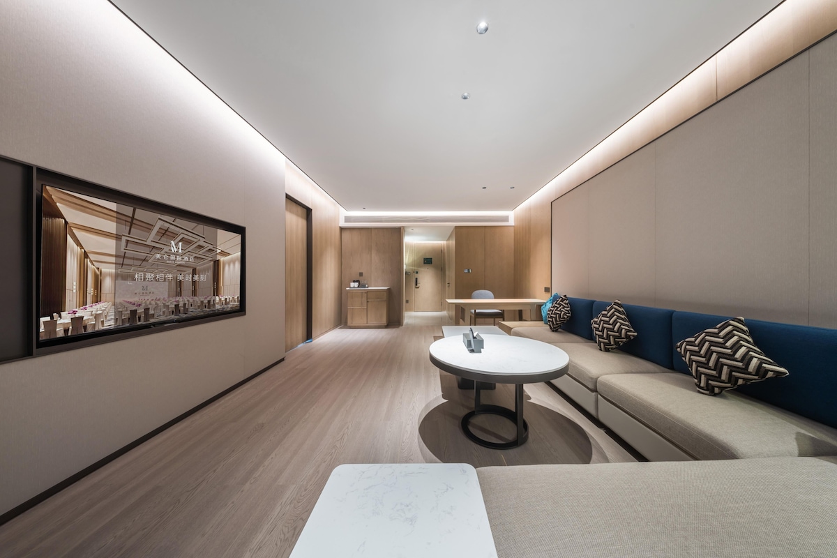 A modern hotel lobby with a central seating area, a reception desk, and a large framed artwork on the wall.