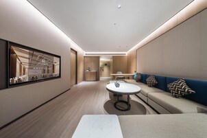 Un moderno vestíbulo de hotel con una zona de estar central, una recepción y una gran obra de arte enmarcada en la pared.