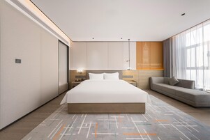 Una habitación de hotel moderna con una cama grande, un sofá y una mesita de noche con lámpara.