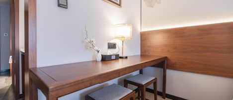 A hotel room with a wooden desk, two matching chairs, a lamp, a framed picture, and a thermostat on the wall.