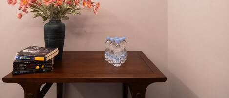 A wooden table with a vase of pink flowers, a stack of books, and six water bottles.