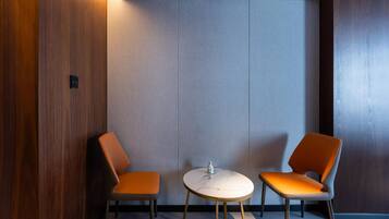 A modern room with two orange chairs and a small round table, featuring a wooden panel wall and a grey panel wall.