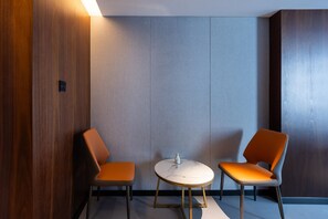 A modern room with two orange chairs and a small round table, featuring a wooden panel wall and a grey panel wall. - Madison Hotel Jinan Suncun Chunhui Road (Jinan)