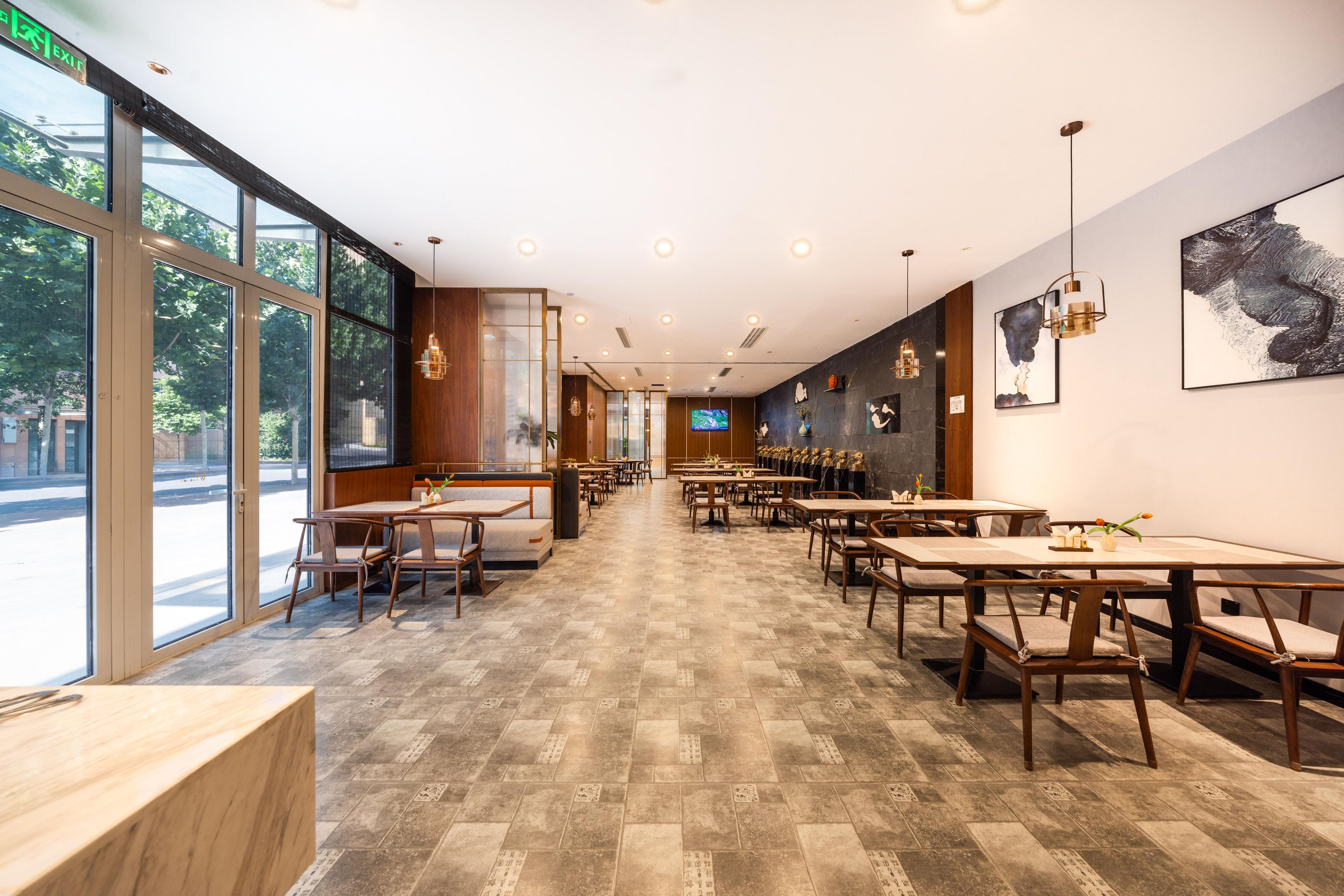A spacious restaurant with long tables and chairs, large windows, and artwork on the walls.