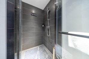 A modern bathroom with dark tiles, a glass shower enclosure, and a visible towel rack. - Madison Hotel Jinan Suncun Chunhui Road (Jinan)
