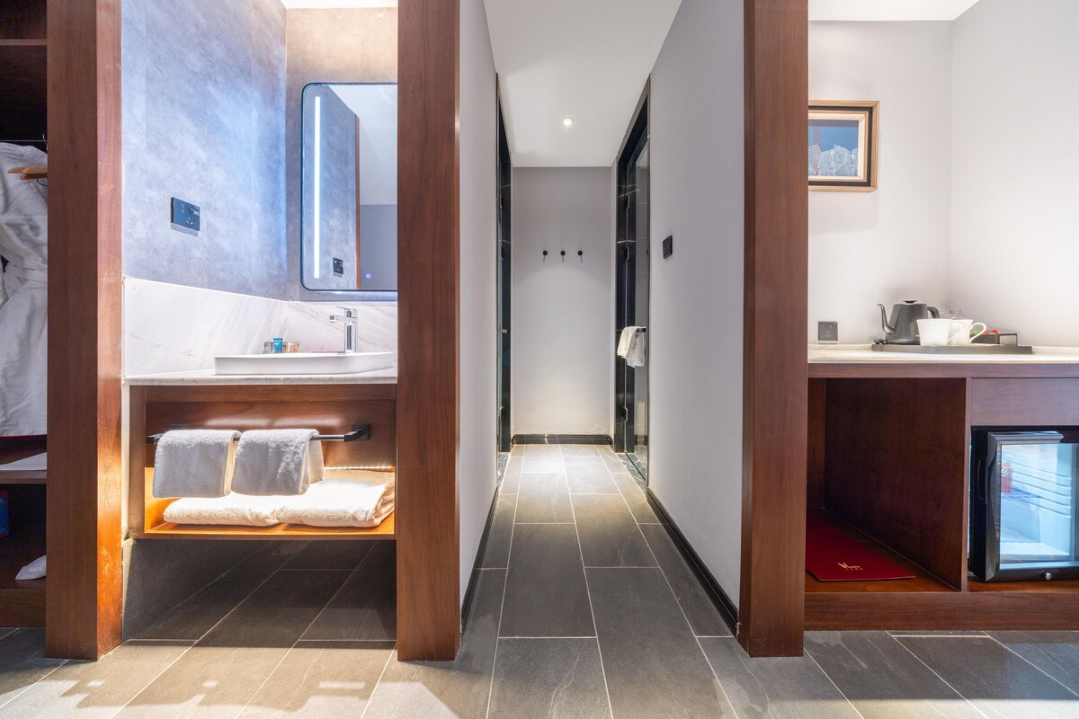 A modern bathroom with a vanity, a mirror, a shower, and a small refrigerator.