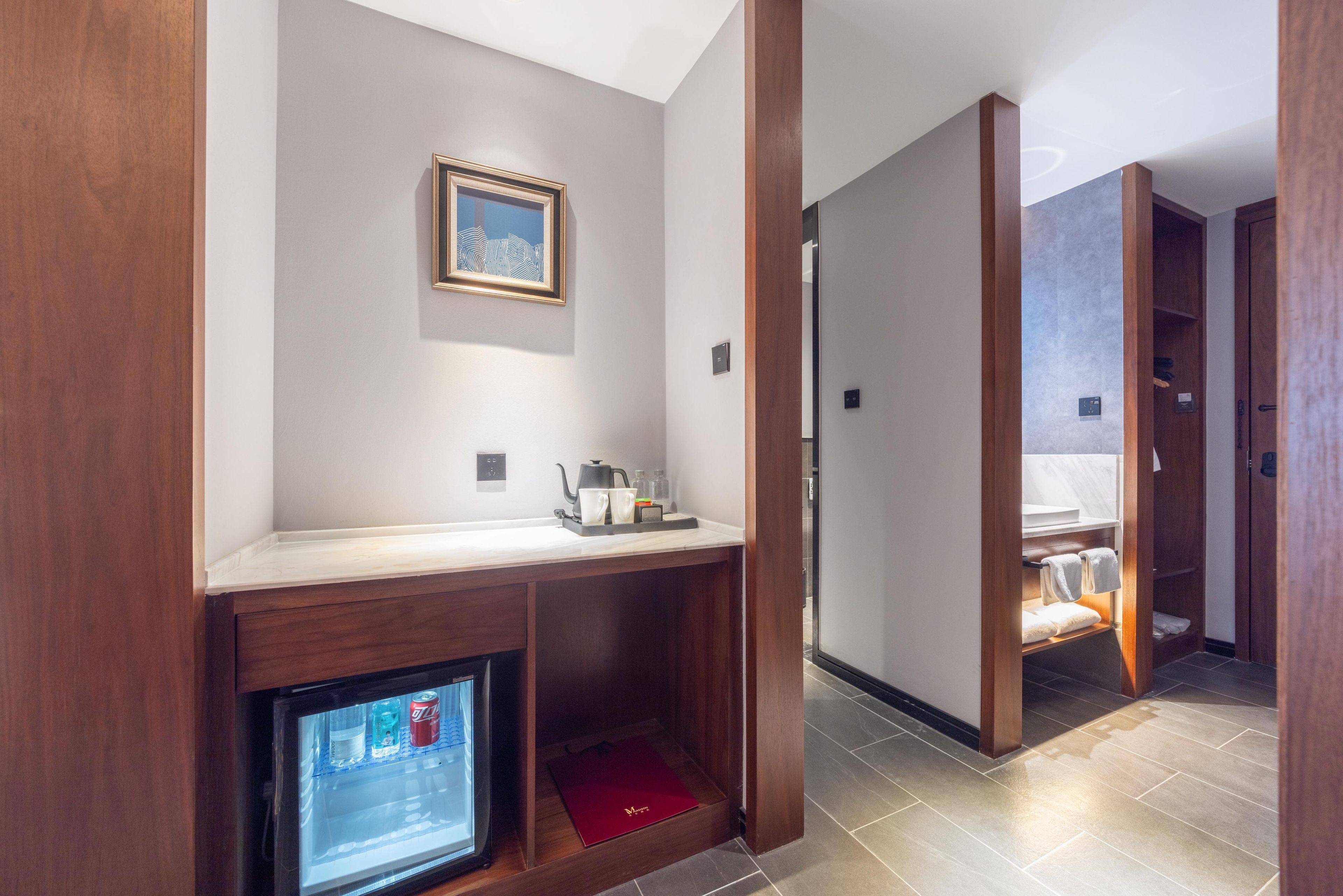 A hotel room with a wooden console table, a framed picture, a digital screen, and a red folder.