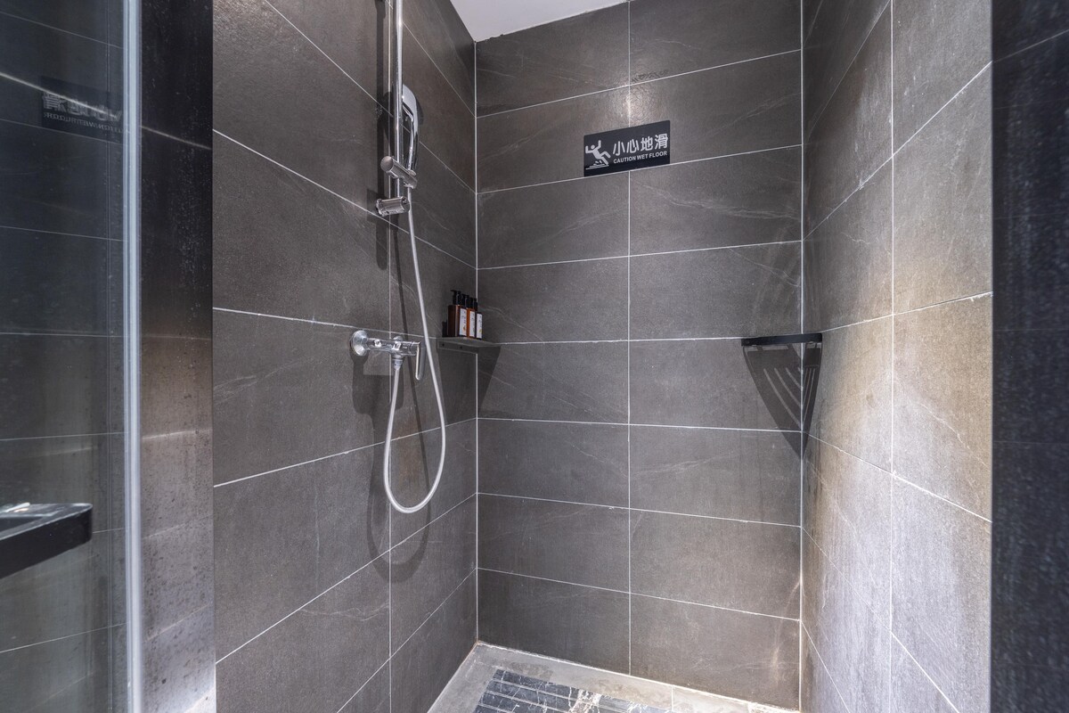 A modern shower area with dark tiles, a glass door, and a caution wet floor sign.