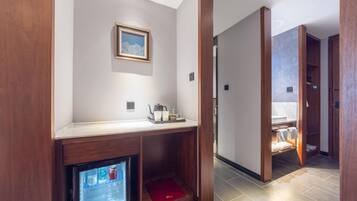 A hotel room with a wooden console table, a framed picture, a digital screen, and a red folder.