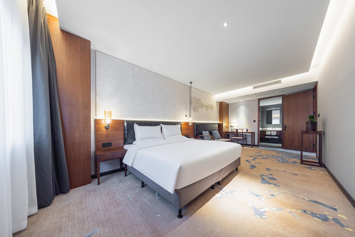 A modern hotel room with a large bed, bedside tables, a desk, and a mirror.