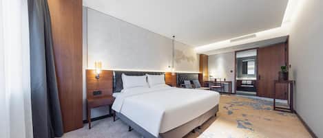 A modern hotel room with a large bed, bedside tables, a desk, and a mirror.