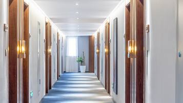 Un couloir d’hôtel avec des portes en bois, des appliques murales et un sol recouvert de moquette.