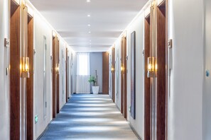 A hotel corridor with wooden doors, wall-mounted lights, and a carpeted floor. - Madison Hotel Jinan Suncun Chunhui Road (Jinan)