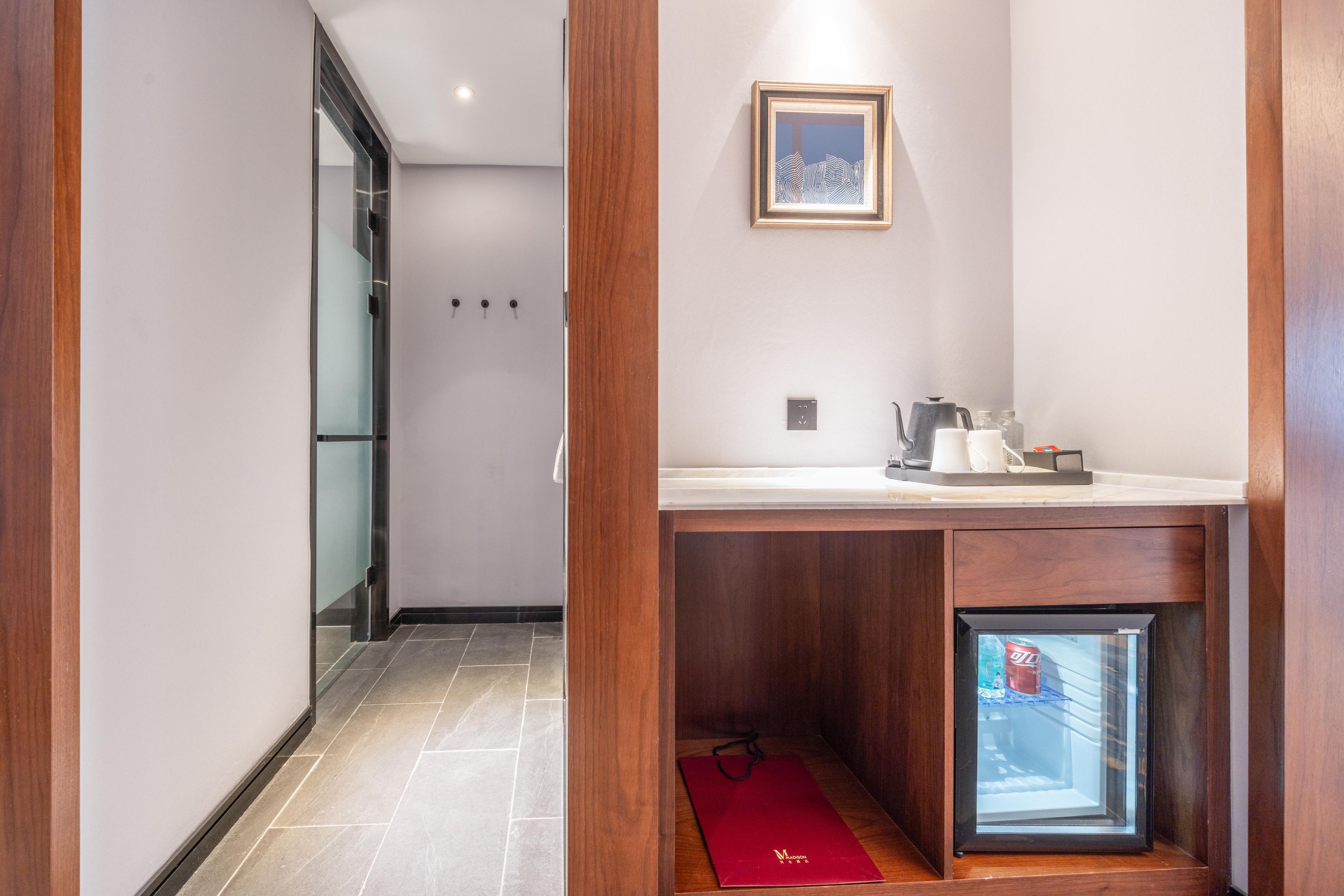 Habitació d'hotel amb un armari de fusta, un refrigerador petit, un quadre amb marc a la paret i un sòl de rajola.