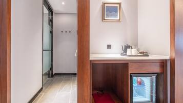 A hotel room with a wooden cabinet, a small refrigerator, a framed picture on the wall, and a tiled floor.