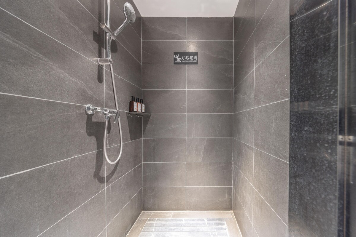 A modern shower area with a glass door, a hand shower, and a wall-mounted shelf with toiletries.