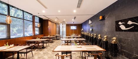 A restaurant with wooden tables and chairs, large windows, and decorative wall art.