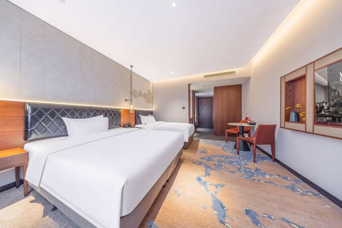 A hotel room with two beds, a small table, and a chair.