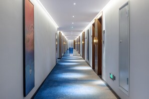 A long, narrow hotel corridor with doors on both sides, a blue carpet, and recessed lighting on the ceiling. - Madison Hotel Jinan Suncun Chunhui Road (Jinan)
