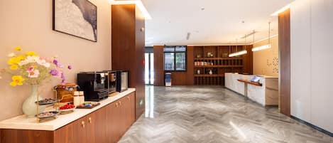 A hotel reception area with a wooden counter, a coffee machine, and a vase of flowers.