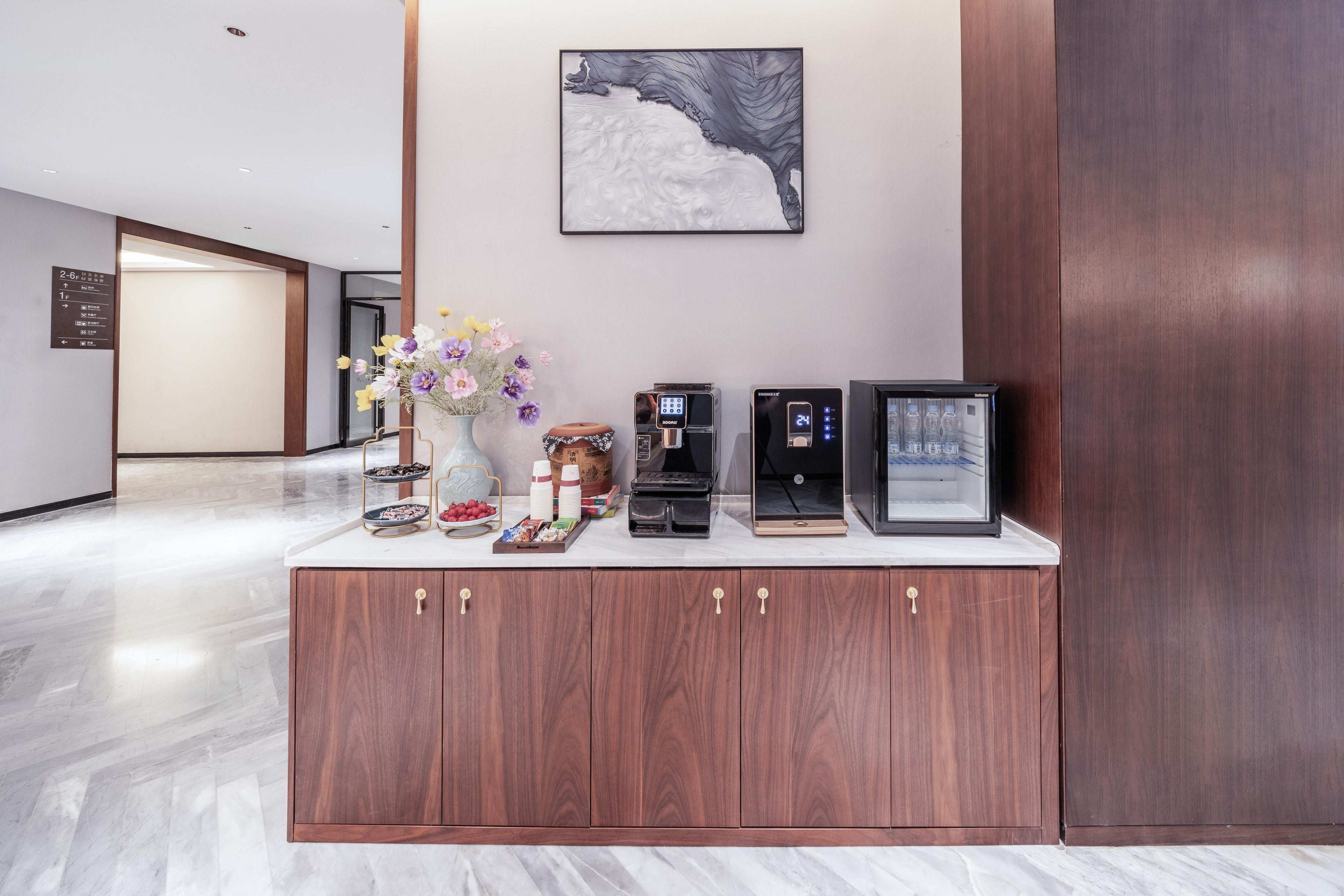 A reception area with a wooden cabinet, a coffee machine, a digital clock, and a framed picture on the wall.