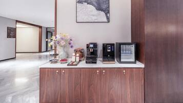 A reception area with a wooden cabinet, a coffee machine, a digital clock, and a framed picture on the wall.
