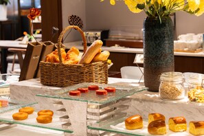 A buffet table with various pastries and bread, a wicker basket, and a vase with flowers. - Madison Hotel Jinan Suncun Chunhui Road (Jinan)