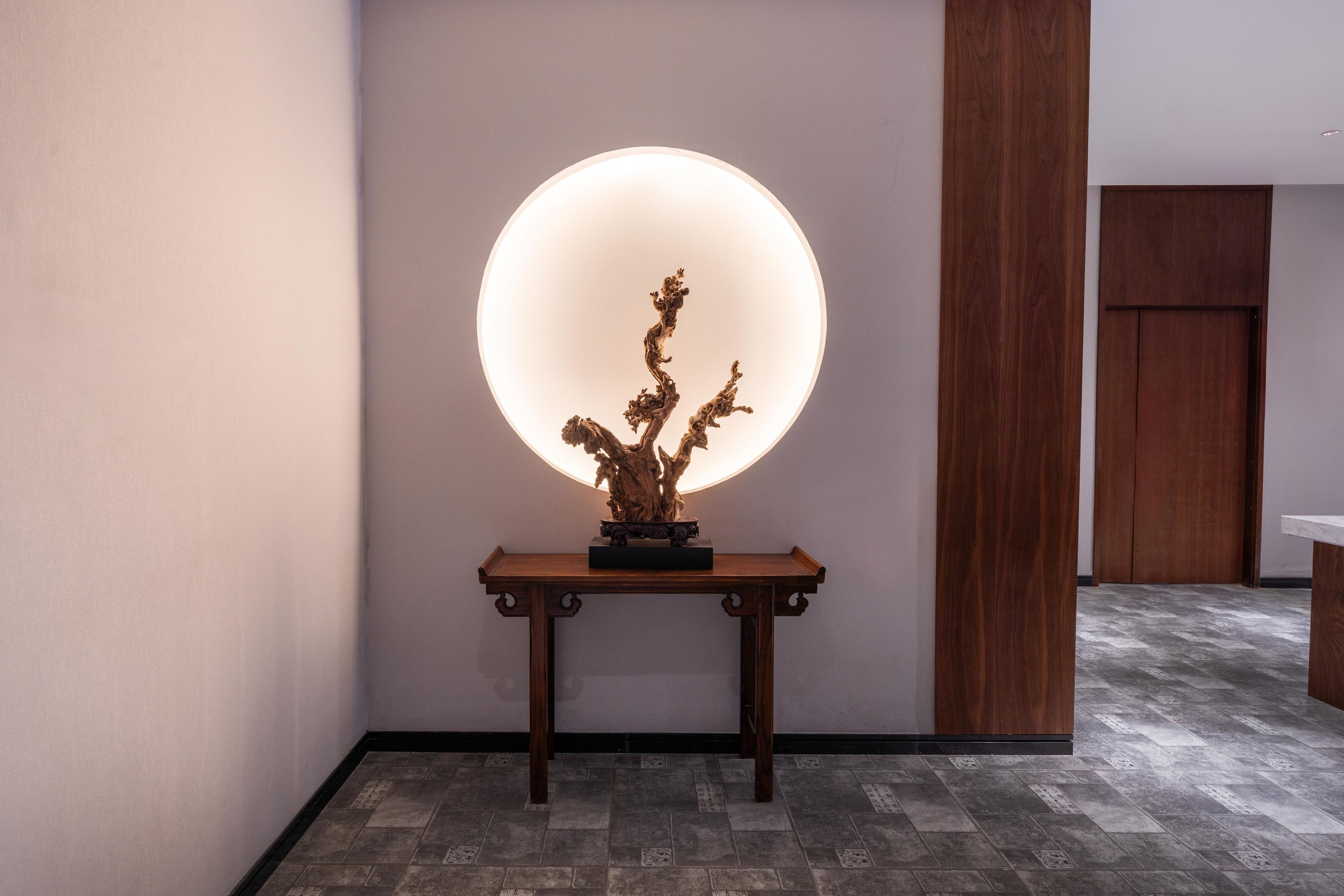 A hallway with a wooden console table featuring a sculpture, a large illuminated sphere, and a wooden door.