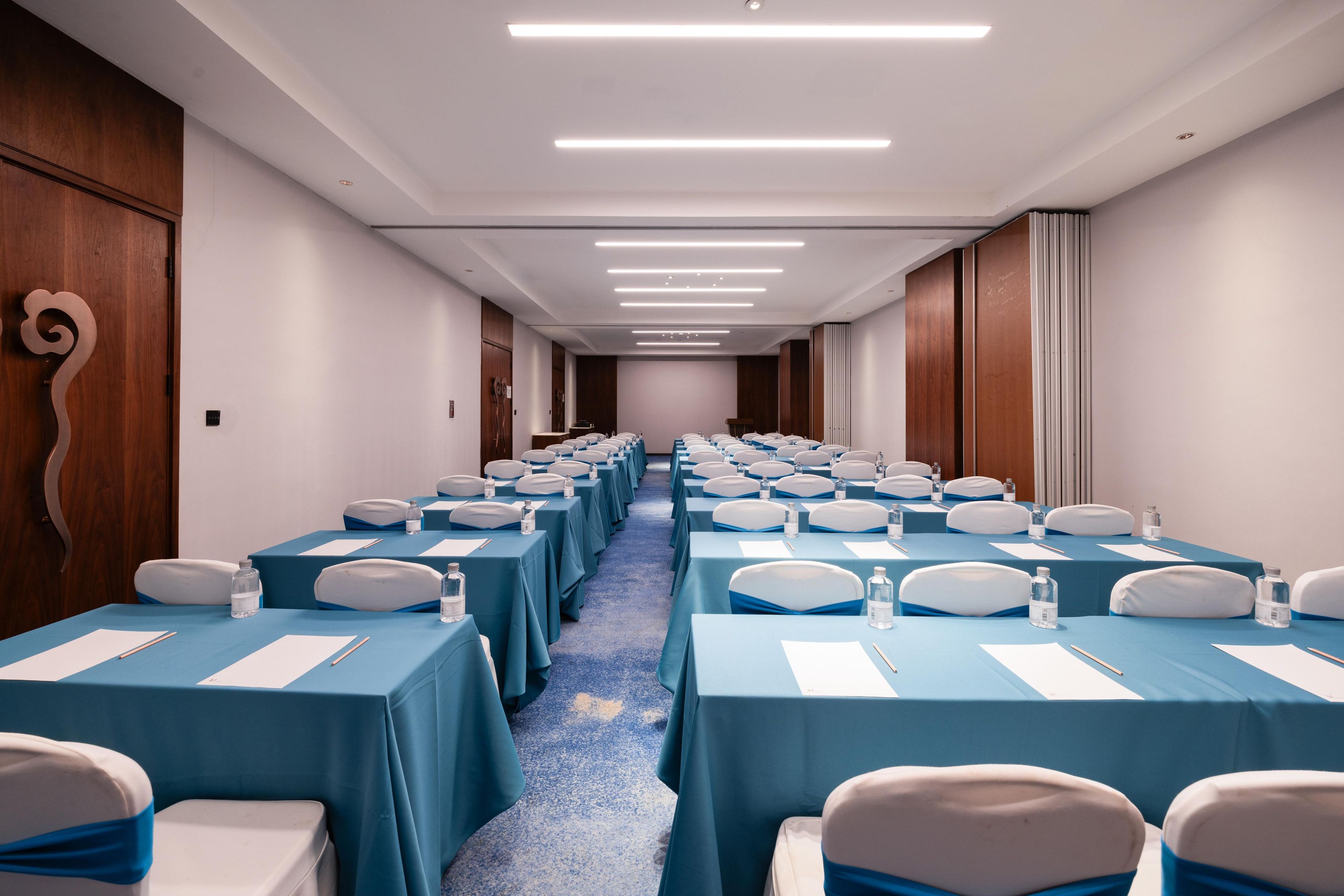 A conference room with rows of tables and chairs, equipped with water bottles and nameplates.