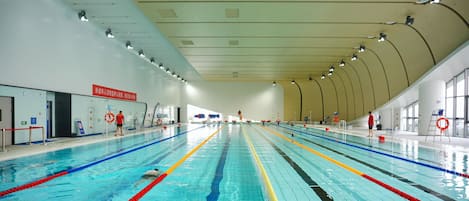 Piscina interior com várias pistas de natação, equipamentos de segurança e boias.