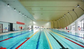 Piscina interior com várias pistas de natação, equipamentos de segurança e boias.