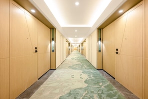 Pasillo de hotel con paneles de madera, iluminación empotrada y alfombra estampada.