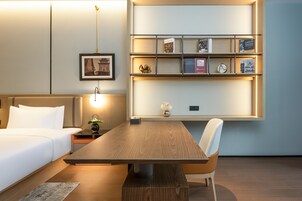 Quarto de hotel moderno com cama de madeira, escrivaninha e estante fixada na parede.