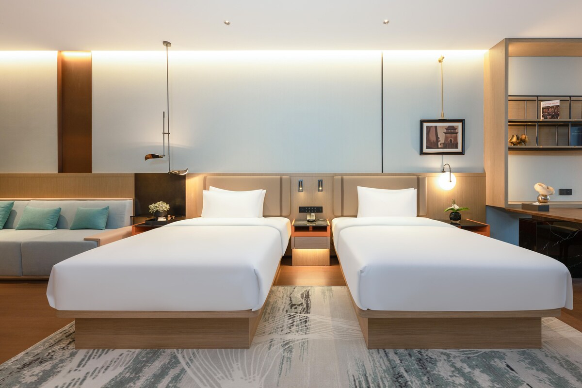 Habitación de hotel con dos camas, un sofá, un escritorio y una estantería.