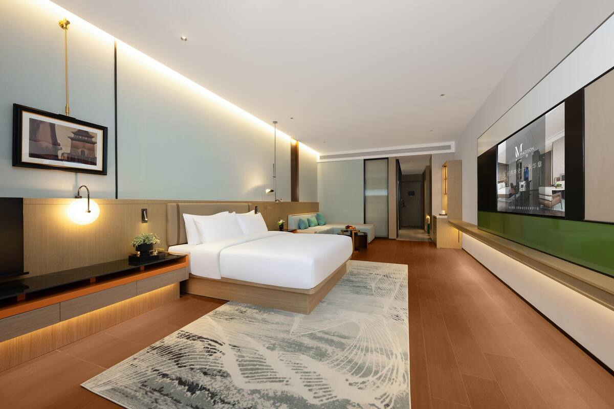 Una habitación de hotel moderna con una cama grande, mesitas de noche, un televisor de pantalla plana y vistas a la ciudad.