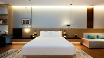 Una habitación de hotel moderna con una cama grande, mesitas de noche, un sofá y un televisor montado en la pared.