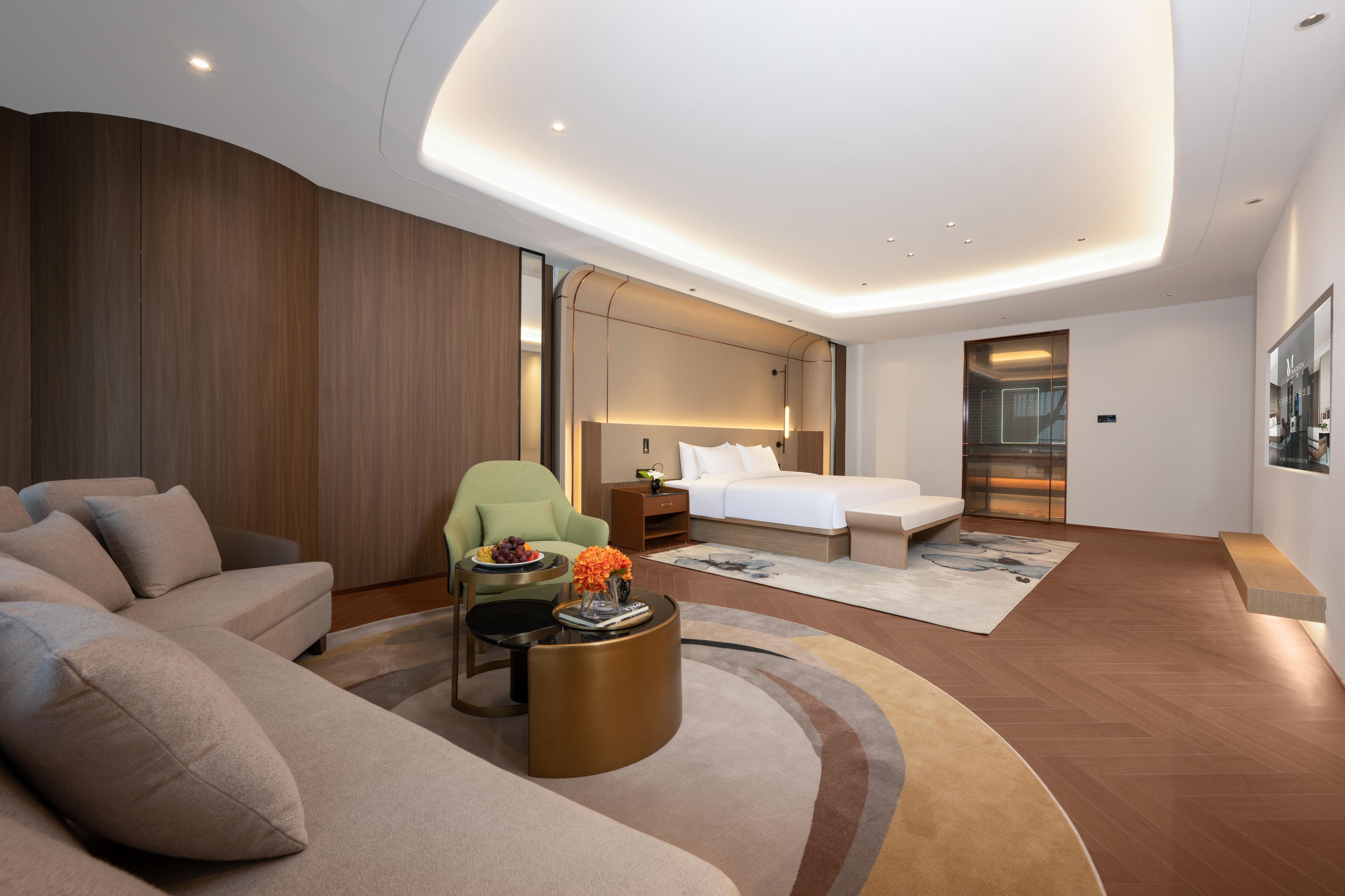 Una habitación de hotel moderna con techo curvo, una cama grande, un sofá, un sillón verde y una mesa de centro.