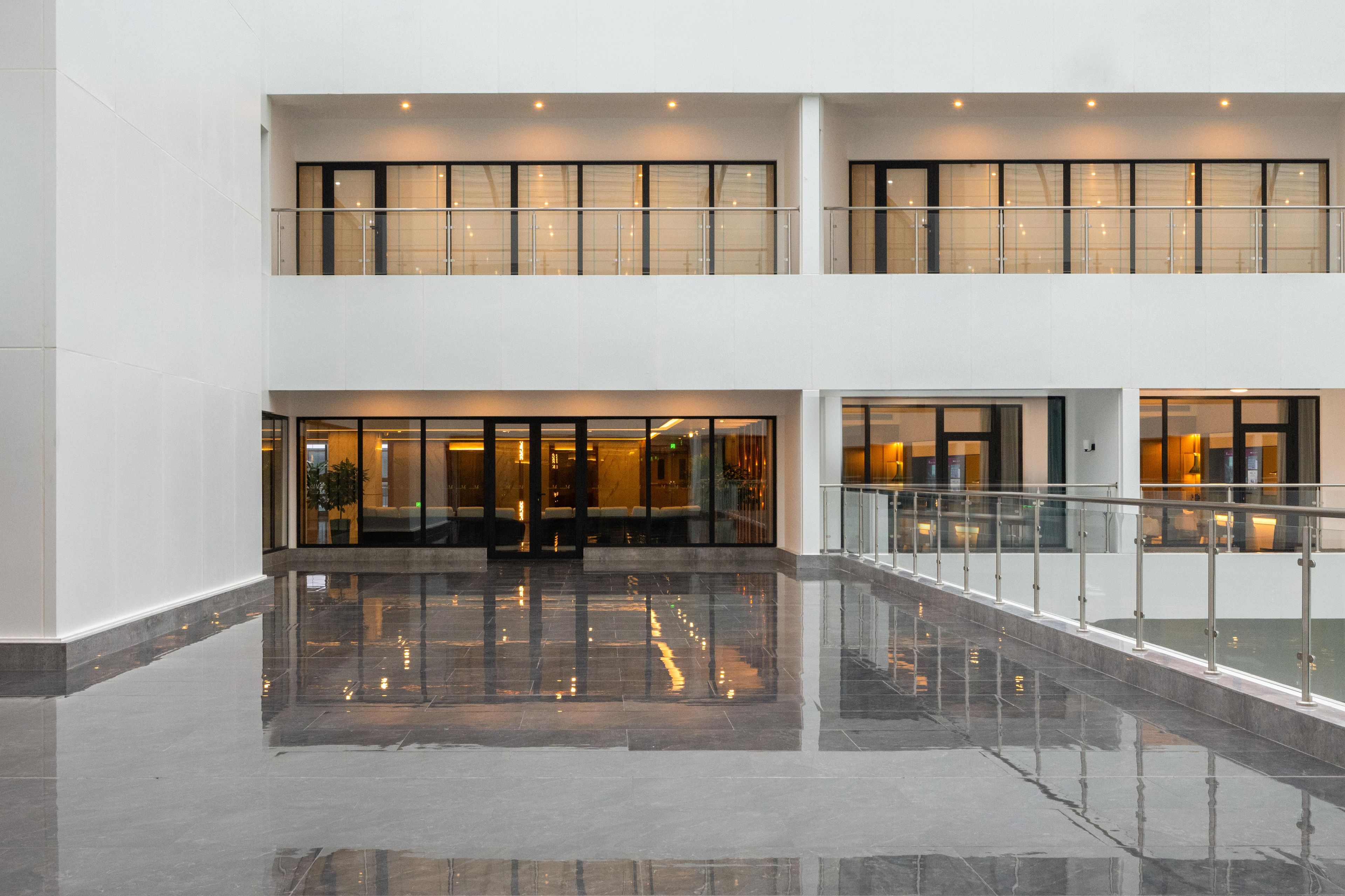 Eine geräumige Lobby mit spiegelndem Boden, einem doppelt hohen Atrium und einem Glasgeländer mit Blick auf die untere Ebene.