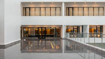 Eine geräumige Lobby mit spiegelndem Boden, einem doppelt hohen Atrium und einem Glasgeländer mit Blick auf die untere Ebene.