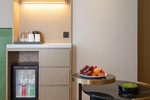 Una kitchenette compacta con refrigerador, una mesita con frutero y cafetera sobre la encimera.