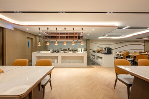 Un área de comedor moderna con una barra central, varias mesas y sillas color naranja.