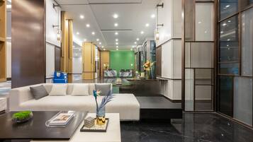 A modern hotel lobby with a white sofa, a coffee table, and a green wall in the background.