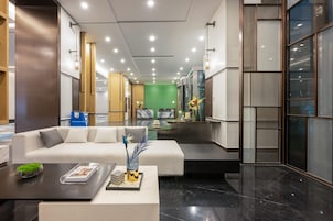 A modern hotel lobby with a white sofa, a coffee table, and a green wall in the background.