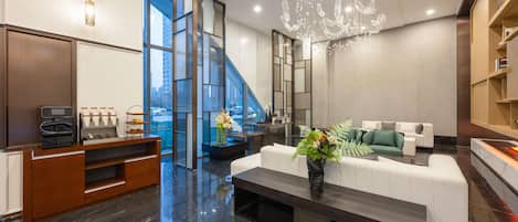A modern lobby with a marble floor, a white sofa, a coffee station, and a staircase leading to an upper floor.