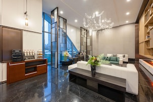 A modern lobby with a marble floor, a white sofa, a coffee station, and a staircase leading to an upper floor.