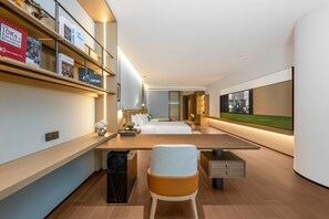 Una habitación de hotel moderna con una cama grande, un escritorio, una silla y una estantería llena de libros.
